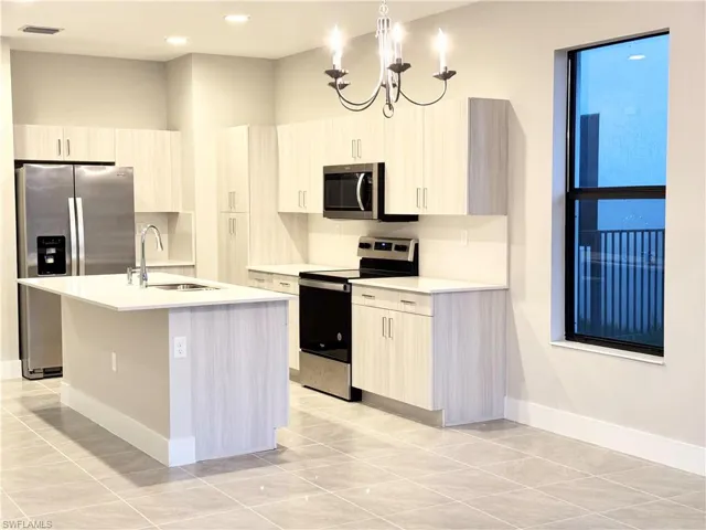 Kitchen with sink, hanging light fixtures, a kitchen island with sink, a notable chandelier, and stainless steel appliances
