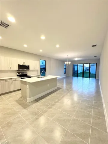 Kitchen with sink, a center island with sink, light tile patterned floors, appliances with stainless steel finishes, and a notable chandelier