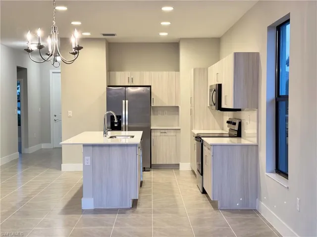 Kitchen with decorative light fixtures, a center island with sink, light brown cabinets, and appliances with stainless steel finishes