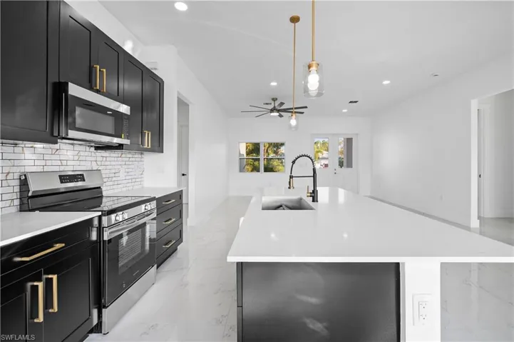 Kitchen with appliances with stainless steel finishes, dark cabinets, light marble finish floors, an island with sink, and recessed lighting