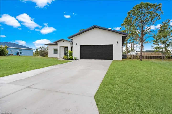 View of front facade featuring stucco siding, a garage, a front lawn, and driveway
