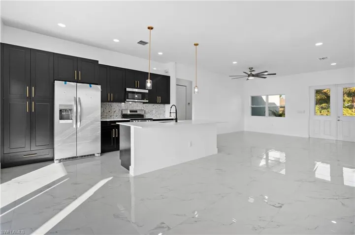 Kitchen with dark cabinetry, light marble finish flooring, appliances with stainless steel finishes, backsplash, and decorative light fixtures