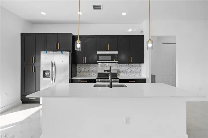 Kitchen featuring light marble finish flooring, dark cabinets, tasteful backsplash, a kitchen island with sink, and pendant lighting
