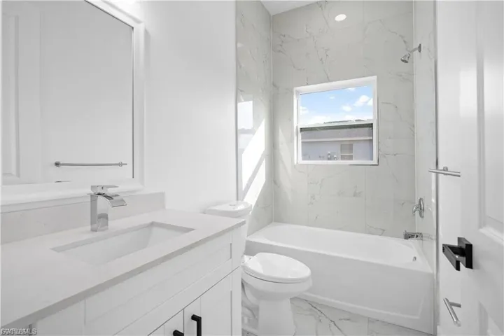 Full bath featuring light marble finish floors, vanity, and shower / bath combination