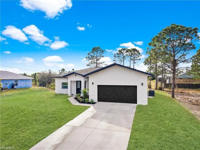 View of front facade featuring stucco siding, a garage, a front lawn, and driveway