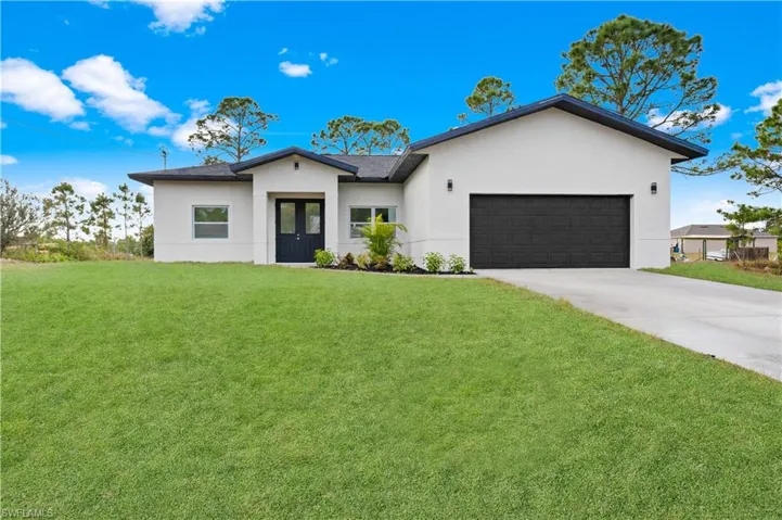 View of front of home with stucco siding, a front lawn, a garage, and driveway