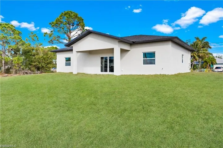 Back of house with stucco siding and a lawn