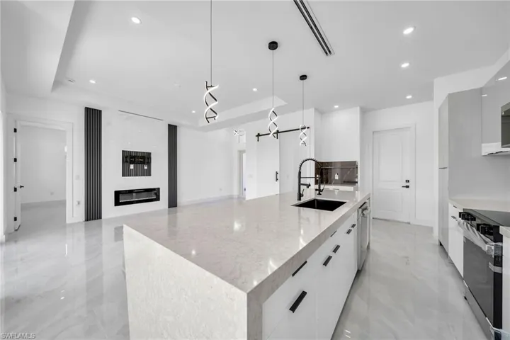 Kitchen featuring pendant lighting, a large island with sink, sink, and white cabinetry