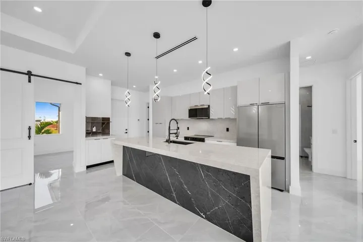 Kitchen featuring hanging light fixtures, sink, white cabinetry, appliances with stainless steel finishes, and a barn door