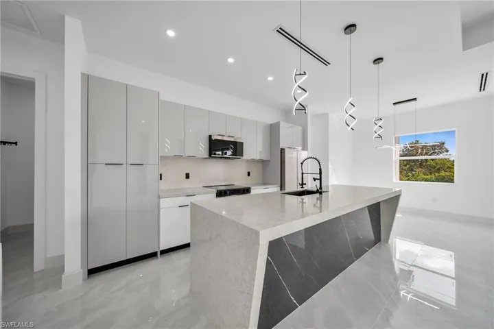 Kitchen with hanging light fixtures, sink, tasteful backsplash, a center island with sink, and stainless steel appliances