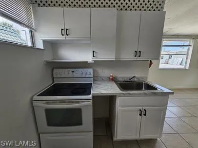 Kitchen featuring white range with electric stovetop, light countertops, white cabinetry, and light tile patterned floors