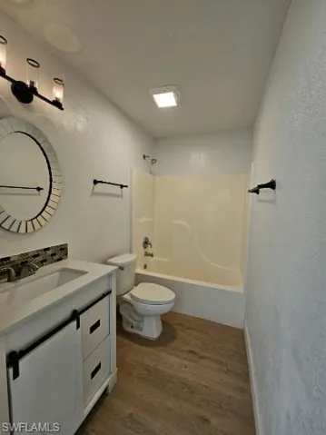 Full bath featuring a textured wall, vanity, dark wood-type flooring, and  shower combination