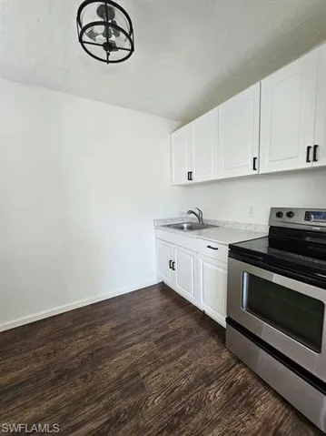 Kitchen with stainless steel electric range, white cabinetry, dark wood finished floors, and light countertops