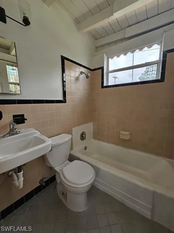 Bathroom with  shower combination, tile walls, light tile patterned floors, and a wood ceiling with exposed beams