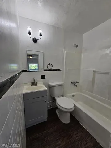 Bathroom with vanity, washtub / shower combination, dark wood-style floors, and tile walls