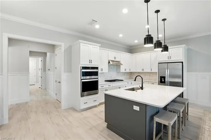 Kitchen with appliances with stainless steel finishes, white cabinets, a breakfast bar area, a kitchen island with sink, and crown molding