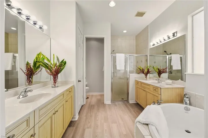 Full bathroom with two vanities, a shower stall, light wood-style floors, a bath, and recessed lighting