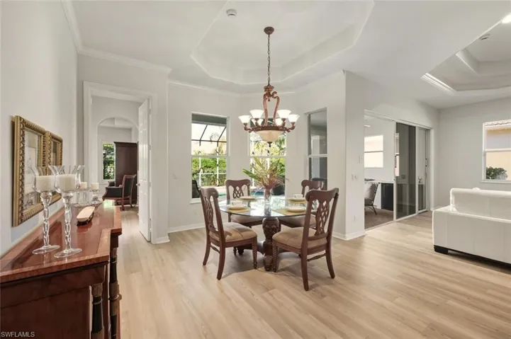 Dining area with a chandelier, a tray ceiling, light wood-type flooring, and crown molding