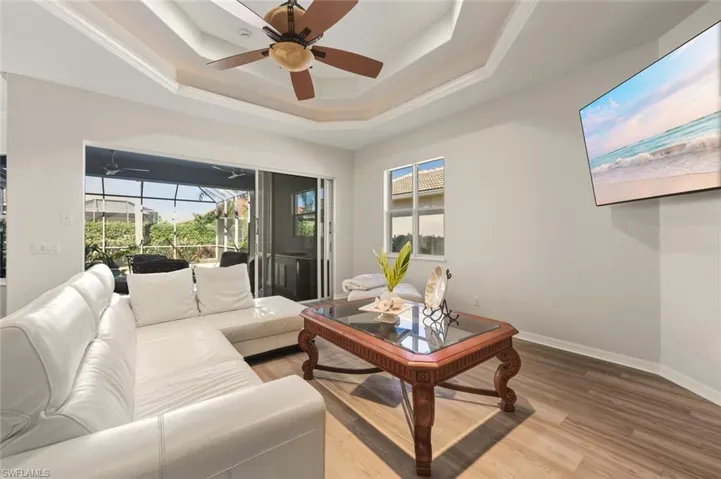 Living room featuring a sunroom, plenty of natural light, light wood-style floors, a raised ceiling, and ornamental molding