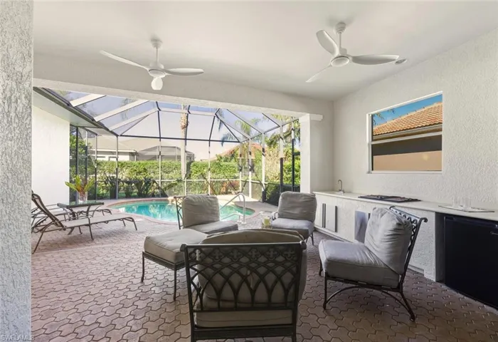 View of patio featuring a sunroom, ceiling fan, an outdoor kitchen, and glass enclosure