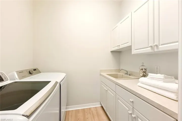 Washroom with cabinet space, light wood-type flooring, and washing machine and clothes dryer