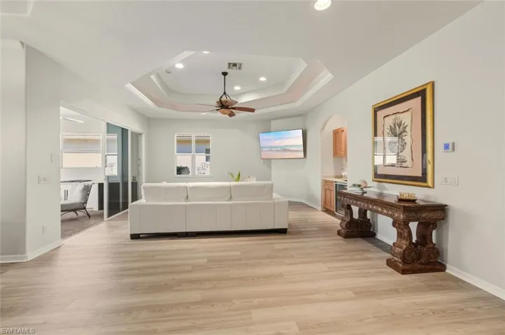 Living area featuring a tray ceiling, light wood-style floors, ceiling fan, and recessed lighting