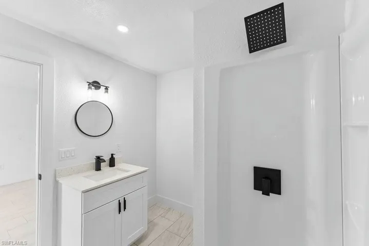 Bathroom with a textured wall, vanity, a shower, and a textured ceiling