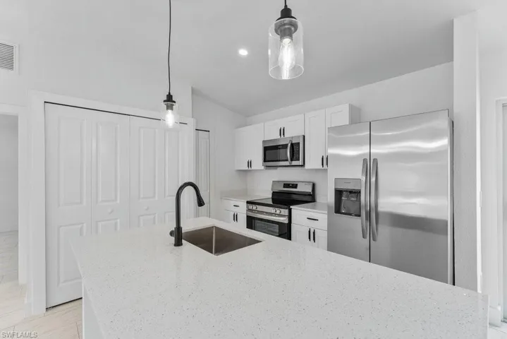 Kitchen with stainless steel appliances, light stone counters, white cabinets, a kitchen island with sink, and pendant lighting