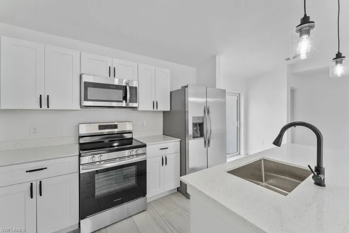 Kitchen featuring stainless steel appliances, light stone countertops, white cabinetry, and decorative light fixtures