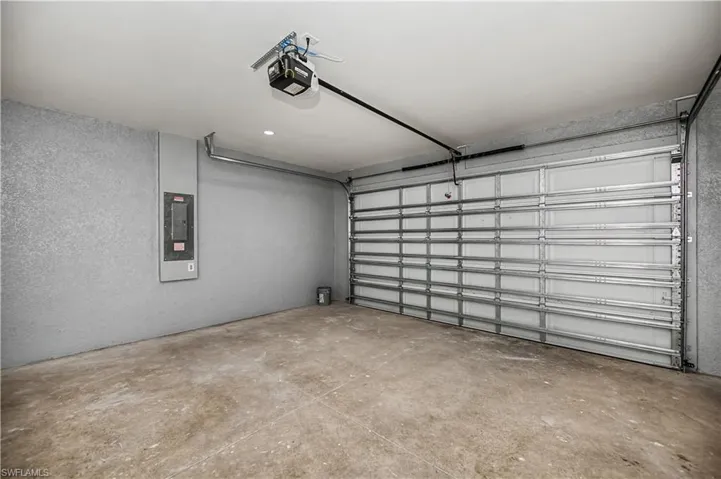 Garage featuring electric panel, a garage door opener, and a textured wall