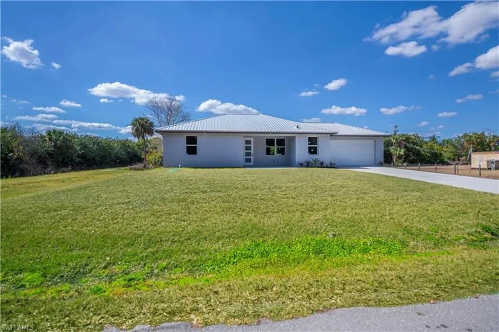 View of front of house with stucco siding, driveway, a front yard, a metal roof, and an attached garage