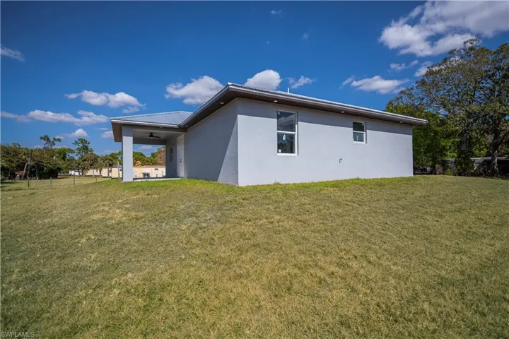 View of side of property featuring stucco siding, a patio area, a ceiling fan, and a metal roof