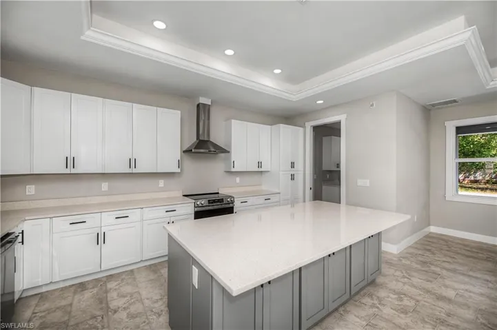 Dual tone kitchen featuring a tray ceiling, stainless steel appliances, dual tone cabinets, a kitchen island, and recessed lighting