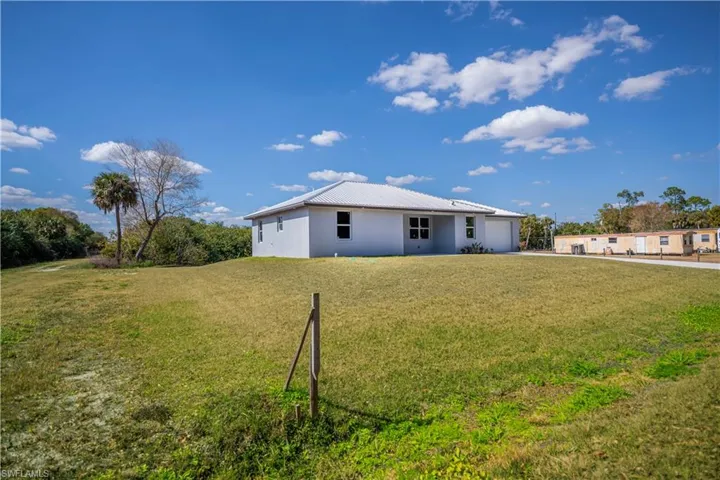 Back of house featuring a yard, stucco siding, a garage, a metal roof, and driveway