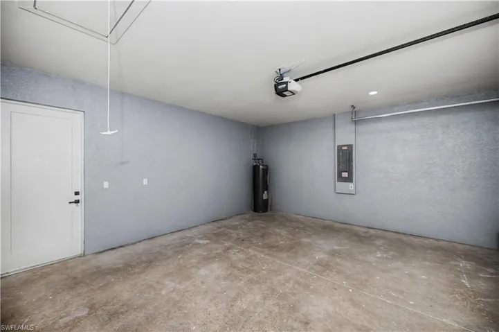 Garage featuring electric panel, electric water heater, and a garage door opener