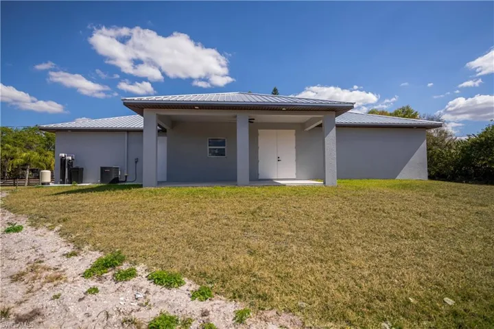 Rear view of property featuring stucco siding, a lawn, and a patio