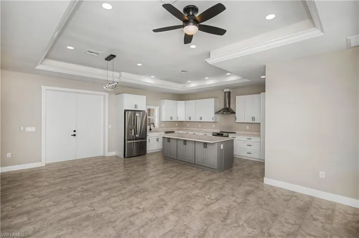 Dual tone kitchen featuring a tray ceiling, dual tone cabinetry, light countertops, stainless steel appliances, and hanging light fixtures