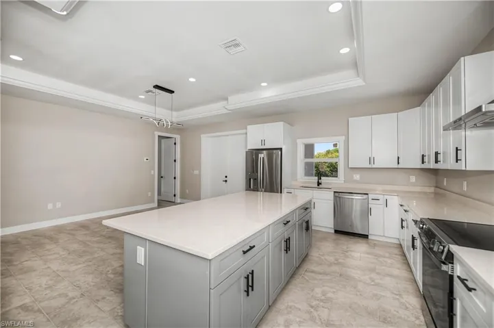 Kitchen with a raised ceiling, two tone color scheme, stainless steel appliances, pendant lighting, and light stone counters