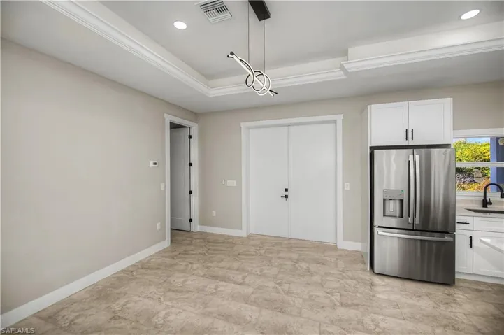 Kitchen featuring white cabinetry, stainless steel fridge with ice dispenser, a tray ceiling, and pendant lighting
