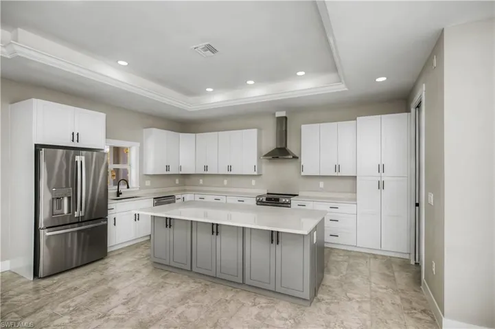 Two tone kitchen with stainless steel appliances, two tone cabinets, a raised ceiling, a center island, and recessed lighting
