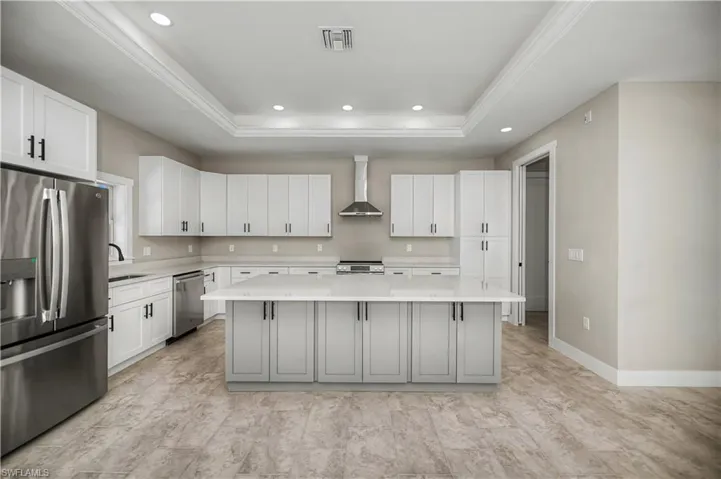 Dual tone kitchen with stainless steel appliances, a kitchen island, recessed lighting, a tray ceiling, and light stone countertops