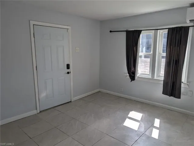 Tiled empty room featuring an AC wall unit