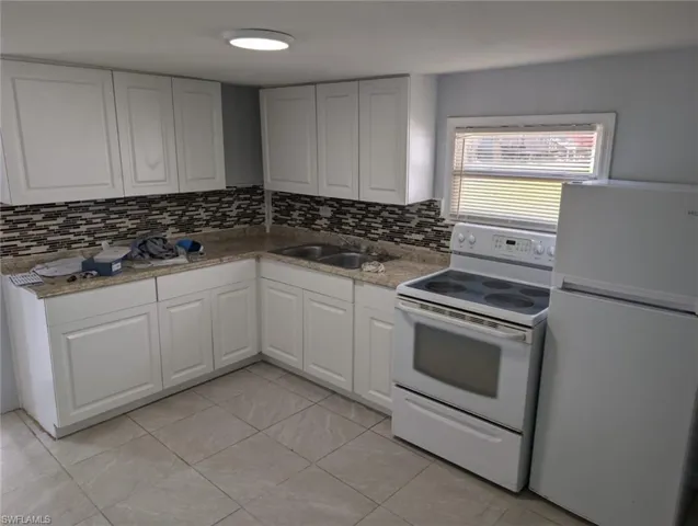 Kitchen featuring white cabinets, tasteful backsplash, and white appliances