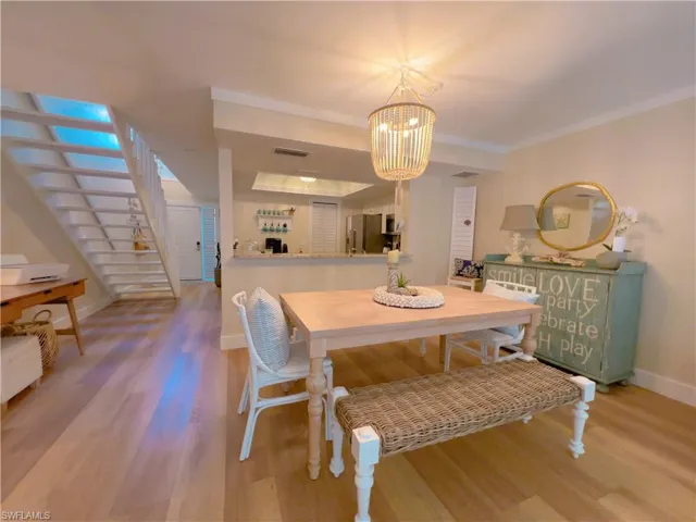 Dining space with wood finished floors, a tray ceiling, stairs, a chandelier, and ornamental molding