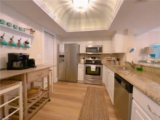 Kitchen featuring white cabinetry, appliances with stainless steel finishes, a tray ceiling, light wood-style flooring, and light stone countertops