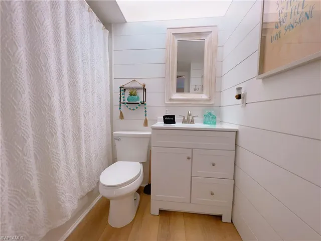 Bathroom with vanity, light wood finished floors, wood walls, and curtained shower