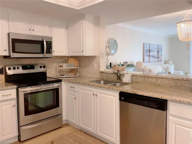 Kitchen featuring appliances with stainless steel finishes, white cabinetry, ornamental molding, light stone counters, and tasteful backsplash