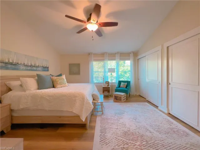 Bedroom featuring lofted ceiling, light wood finished floors, a ceiling fan, and two closets