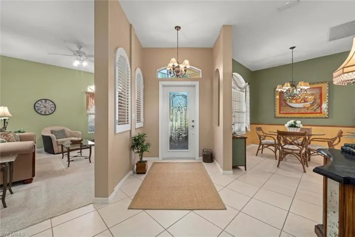 Foyer featuring decorative glass entry door, overhead chandelier, arched windows with plantation shutters, and light-tone tile flooring
