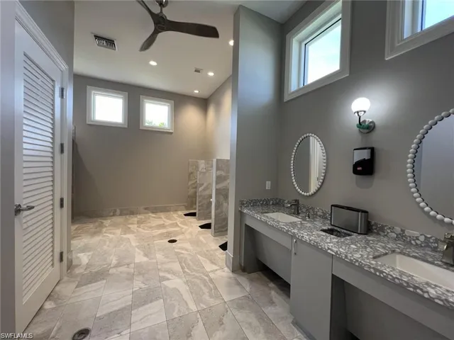 Community full bath with double vanity, healthy amount of natural light, recessed lighting, ceiling fan, and light marble finish floors